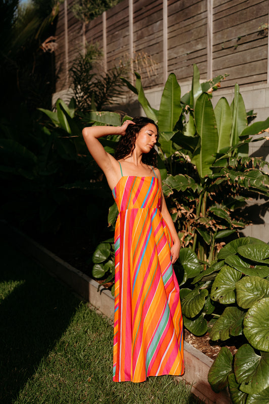 Woman in a colorful dress standing in a garden with large green leaves.