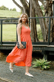 Woman in a coral dress standing outdoors with trees and grass in the background