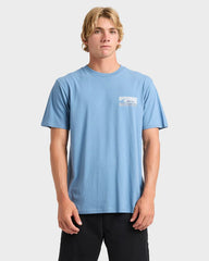 Man wearing a light blue t-shirt with a logo on a white background