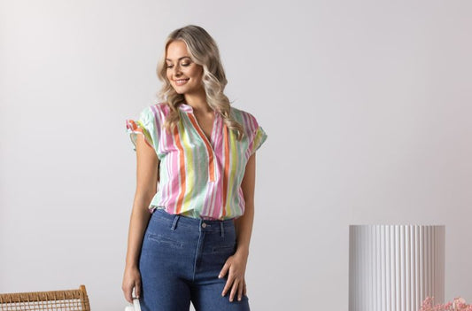 Woman wearing a colorful striped shirt and blue jeans standing in a room with a chair and decorative items.
