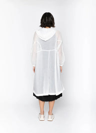 Person wearing a sheer white overcoat with black trim on a white background