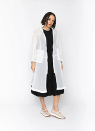 Woman wearing a long, sheer white jacket over a black outfit on a white background