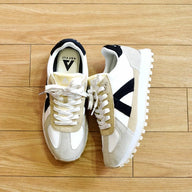 Pair of white and beige sneakers with black accents on a wooden floor.
