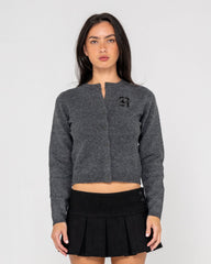Woman wearing a gray cardigan with a logo and a black pleated skirt on a light gray background