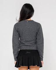Person wearing a gray sweater and black pleated skirt on a light gray background
