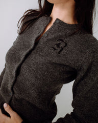 Person wearing a dark gray cardigan with a logo on a plain background