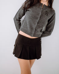 Person wearing a gray sweater and black pleated skirt on a plain background