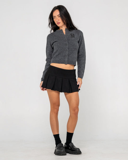 Woman wearing a gray cropped cardi and black pleated skirt on a white background