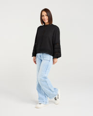 Woman wearing a black sweater and light blue jeans on a white background
