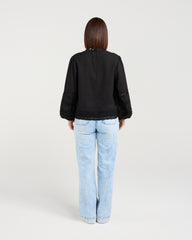 Person wearing a black jacket and light blue jeans on a white background