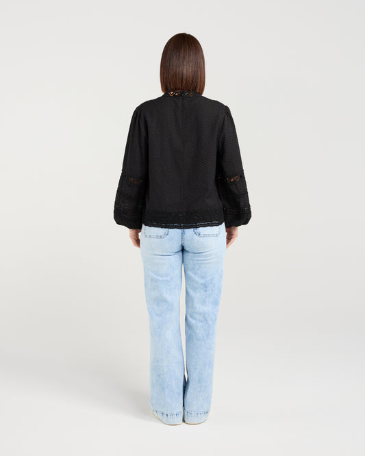 Person wearing a black jacket and light blue jeans on a white background
