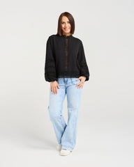 Woman wearing a black sweater and light blue jeans on a white background