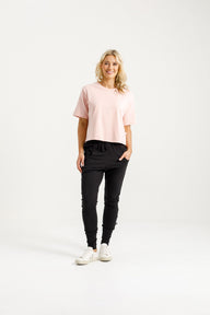 Lady wearing Home-Lee Apartment Pants black with a pink 'X' design & Pink Tee Shirt on a white background