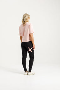 Lady wearing Home-Lee Apartment Pants black with a pink 'X' design & Pink Tee Shirt on a white background