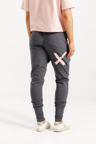 Lady wearing Home-Lee Apartment Pants in Graphite with Blossom X, pink Tee, white sneakers and a white background