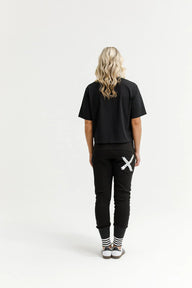 Person wearing a black t-shirt and black pants with a white logo on a white background