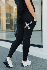 Person wearing black jogger pants with a decorative 'X' design, standing outdoors.