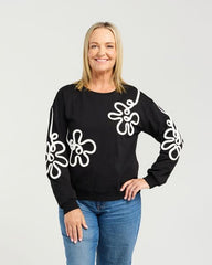 Woman wearing a black sweater with white floral patterns and blue jeans on a white background