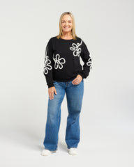 Woman wearing a black sweater with white floral patterns and blue jeans on a white background