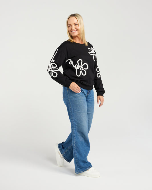 Woman wearing a black sweater with white patterns and blue jeans on a white background