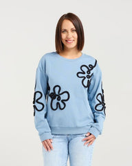 Woman wearing a light blue sweater with black floral patterns and light blue jeans on a white background