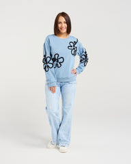 Woman wearing a light blue sweater with black floral patterns and matching pants on a white background
