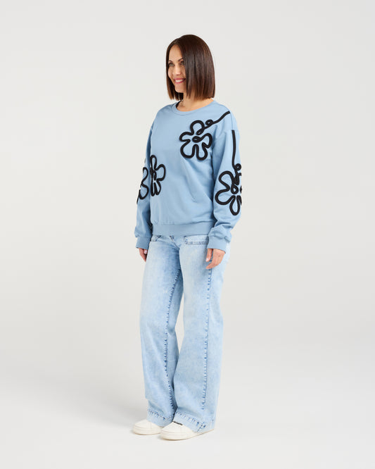 Woman wearing a light blue sweater with black floral patterns and light blue jeans on a white background