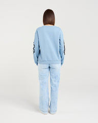 Person wearing a light blue tracksuit with a logo on the back against a white background