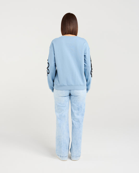 Person wearing a light blue tracksuit with a logo on the back against a white background