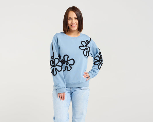 Woman wearing a light blue sweater with black floral patterns and matching pants on a white background