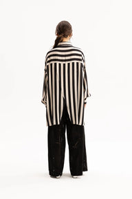 A model viewed from the back wearing a black and cream vertical striped shirt and black wide-leg pants against a plain white studio background.