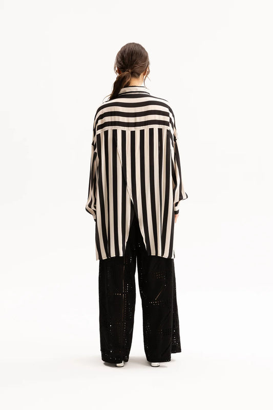 A model viewed from the back wearing a black and cream vertical striped shirt and black wide-leg pants against a plain white studio background.