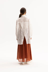 Woman wearing a white lace top and rust-colored skirt on a white background