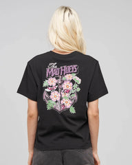 A woman viewed from behind wearing a black graphic t-shirt with a large floral and anchor design on the back, featuring the text 'The Mad Hueys'.