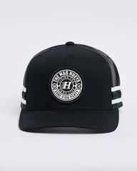 Black trucker cap with white logo and stripes on a light gray background
