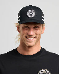 Man wearing a black cap and black shirt with a logo on a gray background