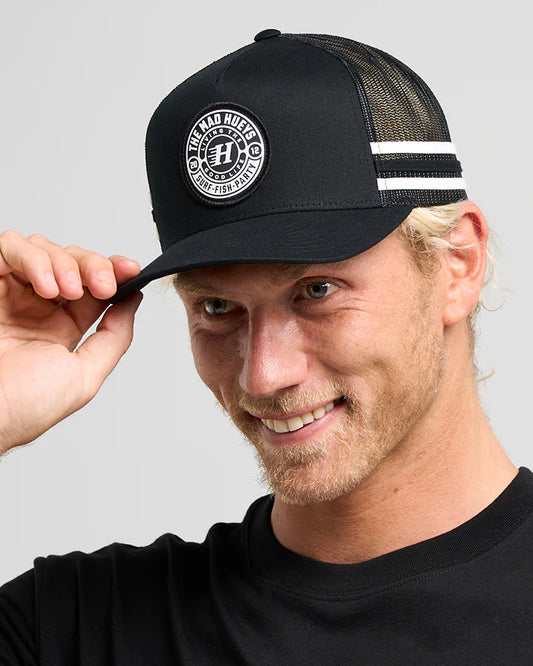 Man wearing a black cap with a logo, against a plain background