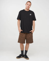 A man wearing a black short-sleeve crewneck t-shirt with a small white graphic logo on the left chest, posed against a light gray studio background.