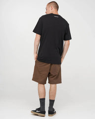 A man wearing a black t-shirt, brown shorts, black socks, and black sneakers, photographed from behind against a light gray studio background.