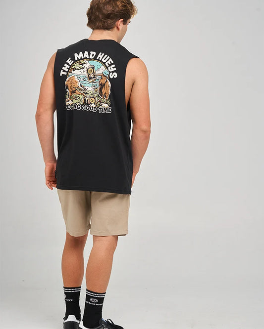 A man wearing a black sleeveless muscle tank top with a large graphic print on the back, paired with beige shorts, black socks, and black sneakers, photographed from behind against a light gray studio background.