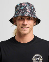 Person wearing a patterned bucket hat and black t-shirt with a logo on a gray background
