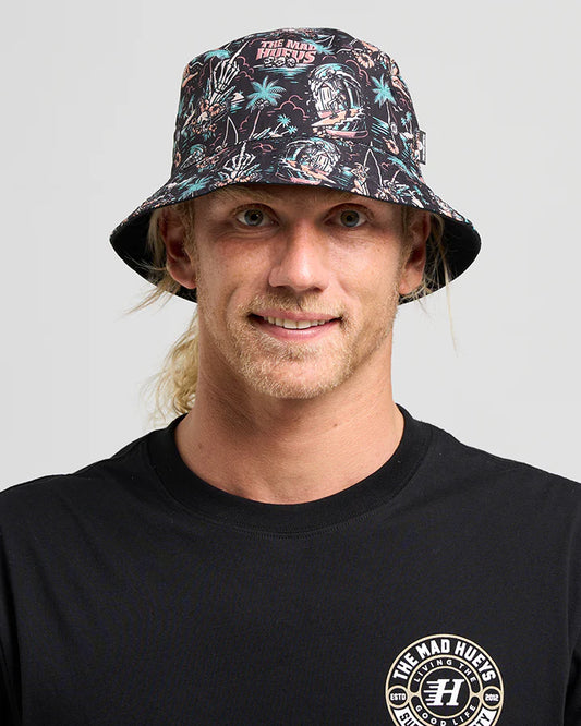 Person wearing a patterned bucket hat and black t-shirt with a logo on a gray background