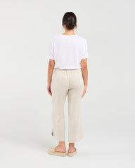 A woman shown from the back wearing a white short-sleeve t-shirt, light beige linen wide-leg cropped pants, and beige espadrille sandals against a plain white studio background.