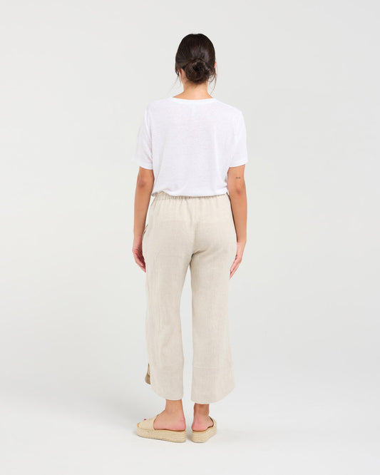 A woman shown from the back wearing a white short-sleeve t-shirt, light beige linen wide-leg cropped pants, and beige espadrille sandals against a plain white studio background.