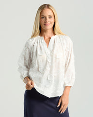 Woman wearing a white blouse with a subtle pattern on a plain background