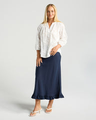 Woman wearing a white blouse and navy skirt on a light gray background