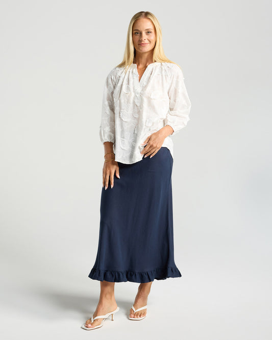 Woman wearing a white blouse and navy skirt on a light gray background