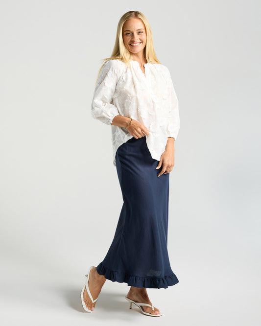 Woman wearing a white blouse and navy skirt on a light gray background