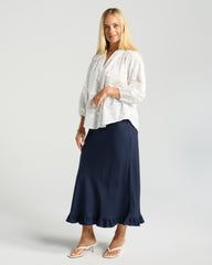 Woman wearing a white blouse and navy skirt on a light gray background