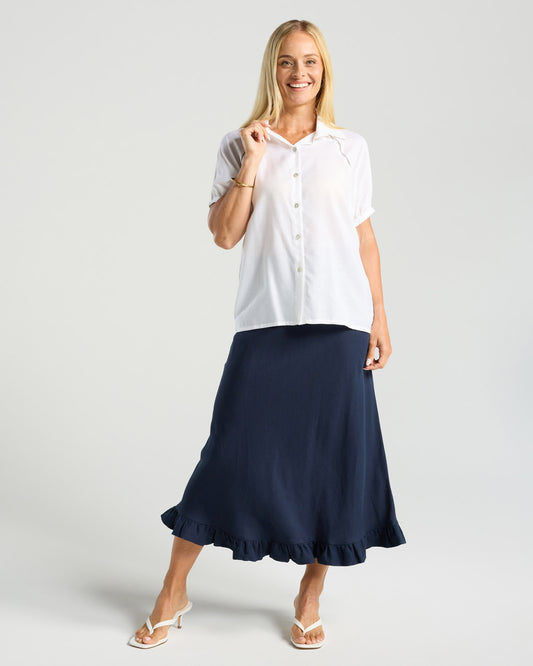 Woman wearing a white blouse and navy skirt on a plain background